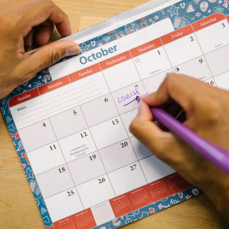 A person writing a reminder on a monthly calendar
