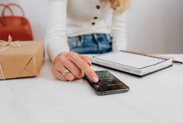 A woman using a smartphone at a desk beside a notebook