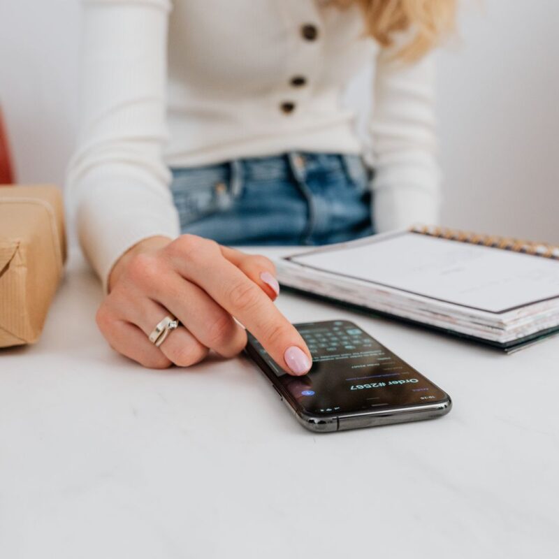 A woman using a smartphone at a desk beside a notebook