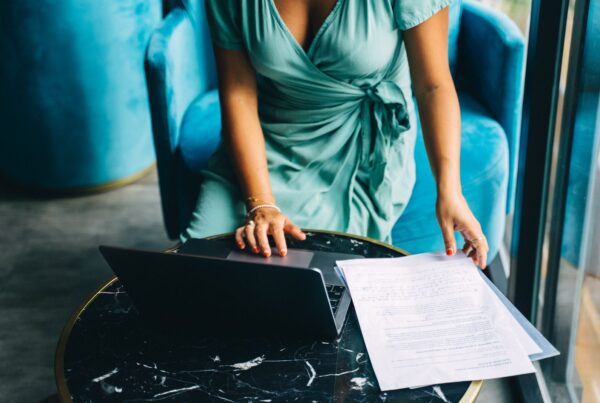 A woman reviewing documents while using a laptop