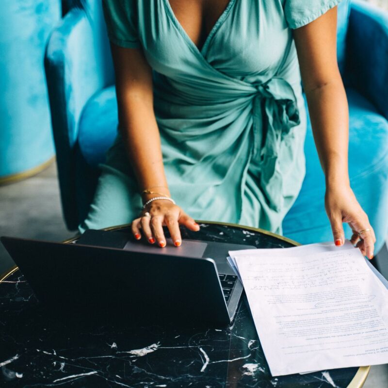 A woman reviewing documents while using a laptop
