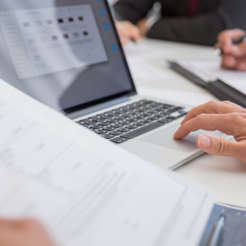 Two people reviewing documents beside a laptop