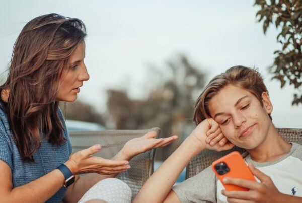 A mother talking with her son while he uses a smartphone outdoors