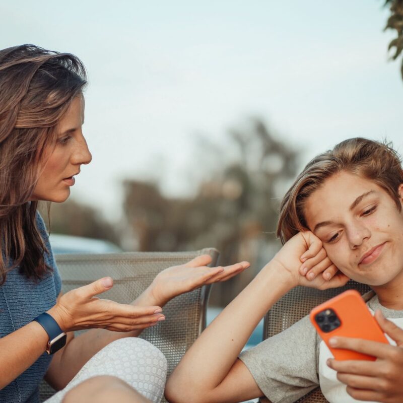 A mother talking with her son while he uses a smartphone outdoors
